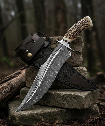 Handmade Damascus steel Bowie knife with stag horn handle and black leather sheath on forest rocks