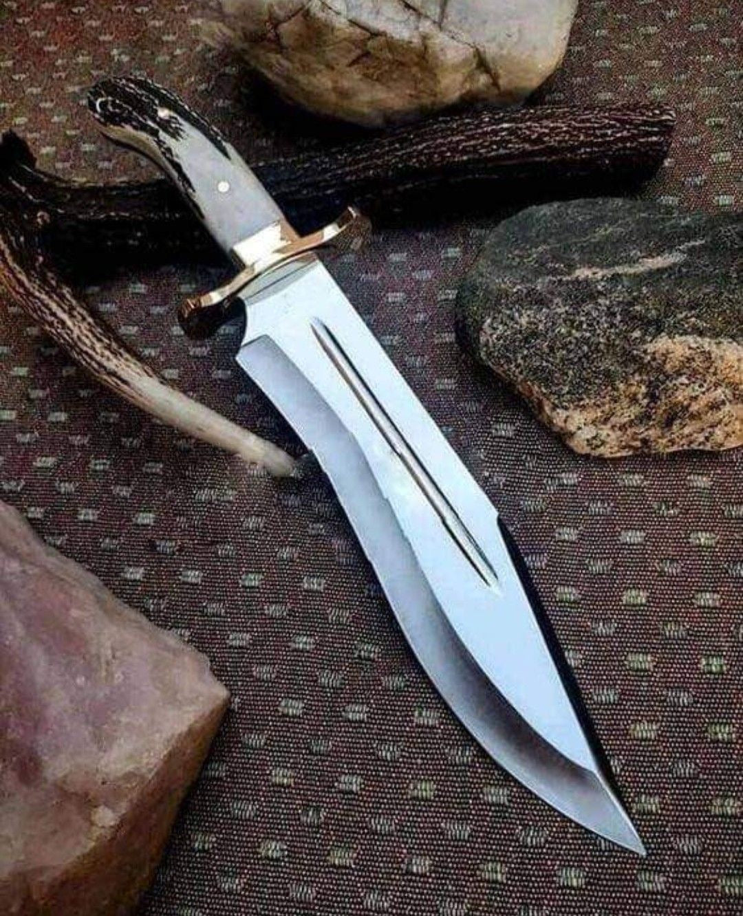 Handmade Bowie knife with stag horn handle and brass guard double fuller blade on fabric surface with rocks