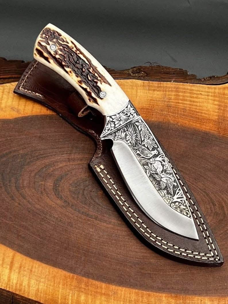 Handmade D2 steel skinner knife with hand engraved eagle and floral blade stag crown handle brass bolster and brown leather sheath on wood slab