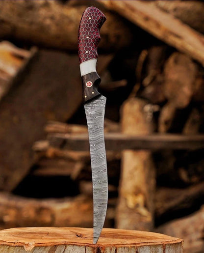 Handmade Damascus steel fish fillet knife with long curved flexible blade red honeycomb G10 handle and black wood bolster standing on wood stump
