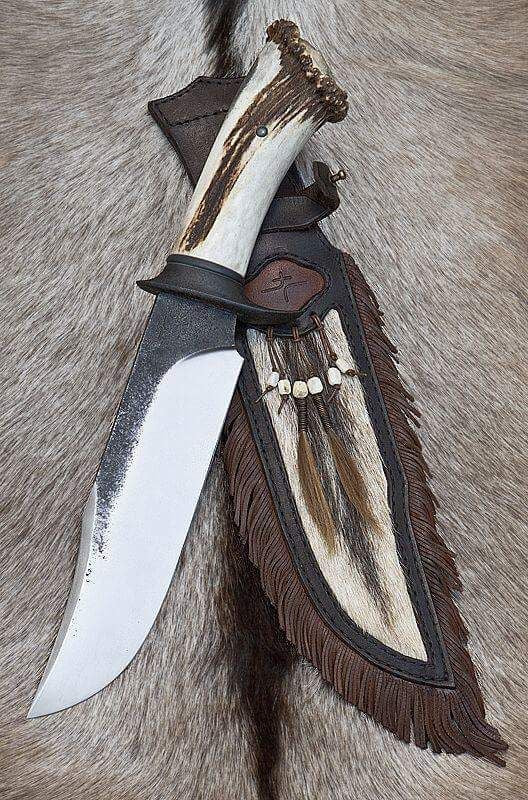 Handmade 1095 high carbon steel Bowie knife with hand-forged black spine mirror polished edge stag crown antler handle black steel guard and fur fringe leather sheath with bone beads on animal fur
