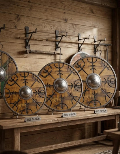 Three round wooden Viking-style shields with metal rims and central bosses, displayed on a wooden shelf against a rustic wood plank wall.