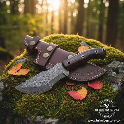 Damascus steel tracker knife with micarta handle and leather sheath on mossy rocks in forest setting