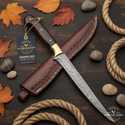 Damascus steel fillet knife rosewood handle flat lay on dark rustic wood with HS Knives Store hang tag attached fishing rope river stones