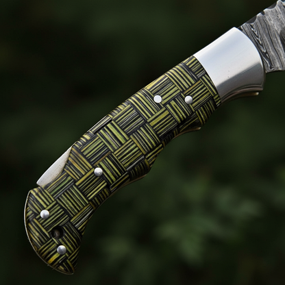 Close-up macro of green black woven composite handle with steel bolster and pins on Damascus folding knife
