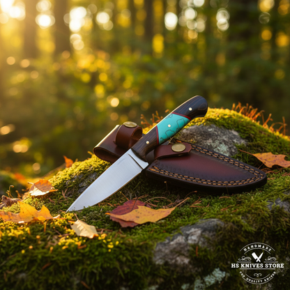 Carbon steel skinner knife with wood turquoise resin handle and dark burgundy leather sheath on mossy rocks in forest setting