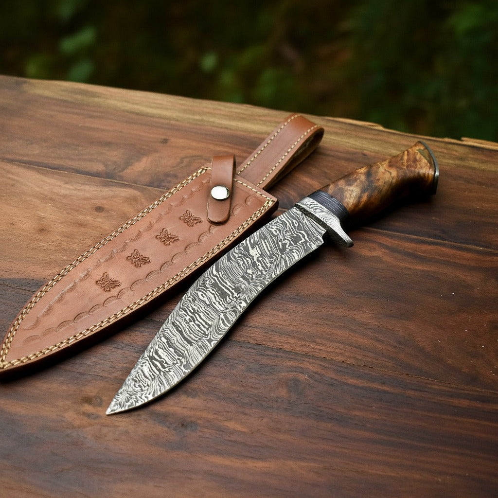 A fixed-blade knife with a patterned steel blade and a brown wood-grain handle, placed on a dark wooden surface next to a brown leather sheath.