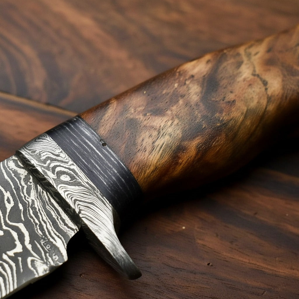 Close-up of a knife with a patterned Damascus-style blade and a richly figured brown wood handle, resting on a dark wood surface.