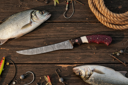 Damascus fillet knife with red honeycomb handle flat lay on dark rustic wood with fresh fish fishing rope and tackle accessories