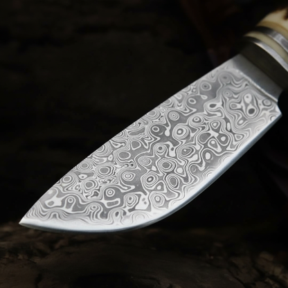 Macro detail of hand-forged Damascus steel blade showing bold swirling circular pattern and razor sharp edge on hunting knife