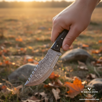 Hand gripping black Micarta handle Damascus tracker knife with serrated spine in outdoor action shot