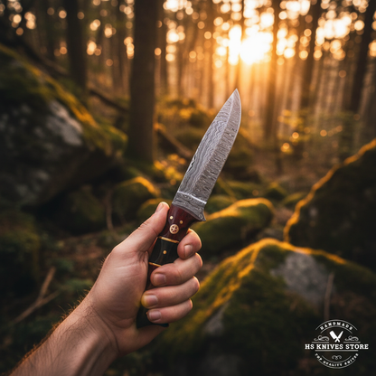Hand gripping red black buffalo horn handle Damascus hunting knife with brass spacers in outdoor forest hunting action shot golden hour light