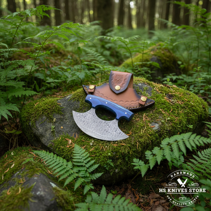 Damascus ulu knife with blue pakkawood handle and crescent leather sheath on mossy rocks in outdoor forest setting