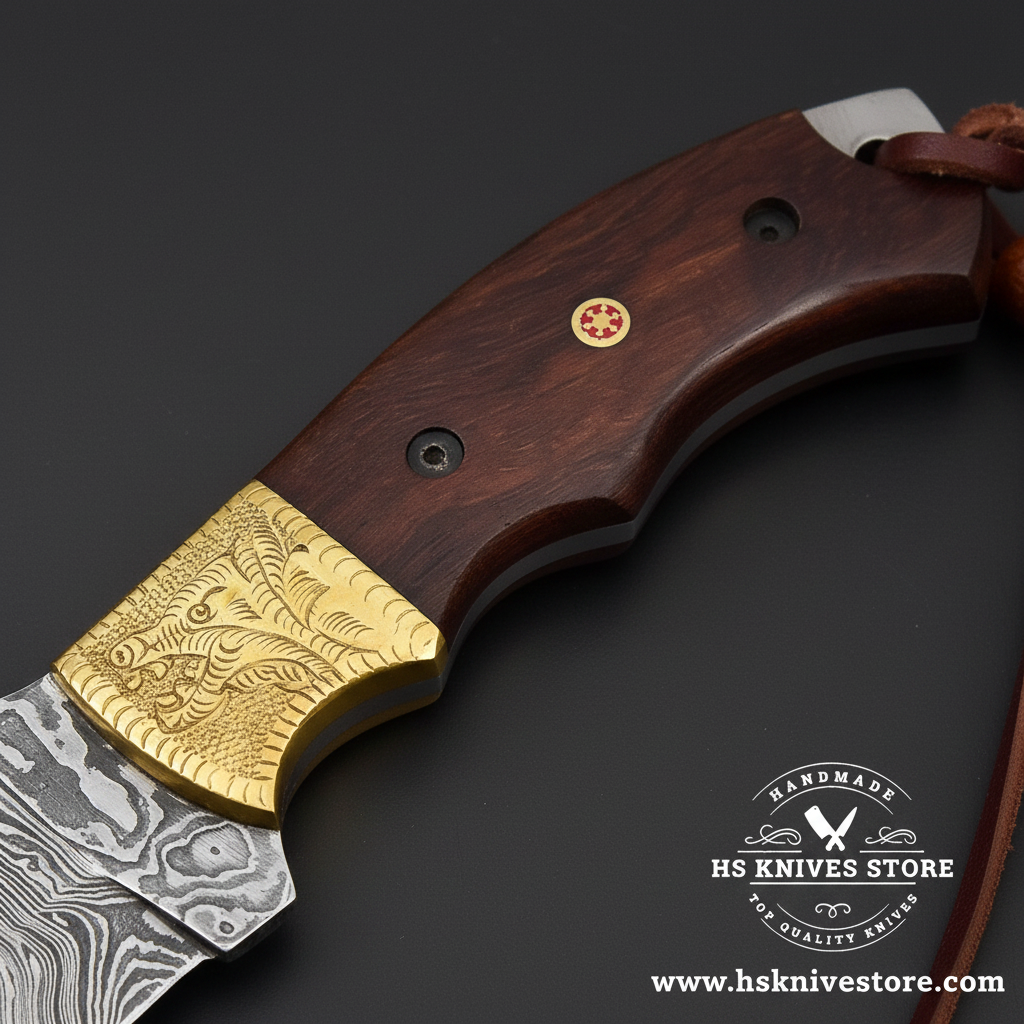 Macro view of dark brown wood handle with black pins ruby pin and engraved brass bolster and leather lanyard on Damascus tracker knife