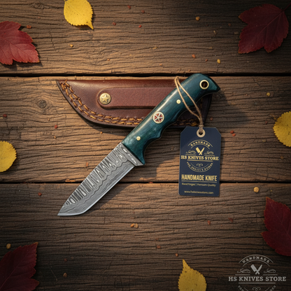 Damascus tanto skinner knife flat lay with teal bone handle hang tag and burgundy leather sheath on dark rustic wood with autumn leaves