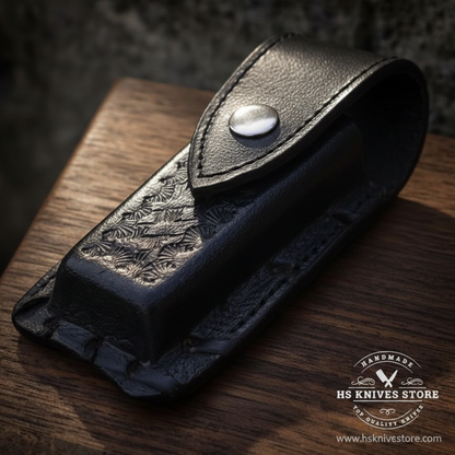 Close-up macro of black leather sheath with floral embossed tooling pattern and silver snap button closure for folding pocket knife