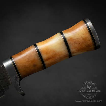 Close-up macro of stacked camel bone handle with warm honey cream tones black spacer rings and rounded pommel on Damascus skinner knife