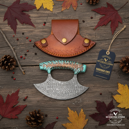 Raindrop Damascus ulu knife flat lay with pine cone teal resin handle and HS Knives Store hang tag on rustic dark wood with autumn leaves