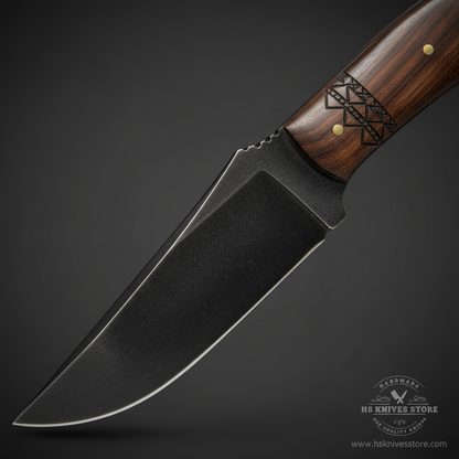 Close-up macro of carbon steel fixed blade knife with black stone-wash coating and matching Norse tribal geometric engraving on walnut handle