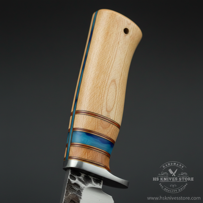Close-up macro of stacked handle maple wood blue resin spacer tan leather spacer rings and silver bolster on hidden tang hunting knife