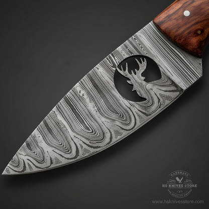 Close-up macro of Damascus steel skinner blade showing swirling Damascus pattern and moose elk silhouette etching detail