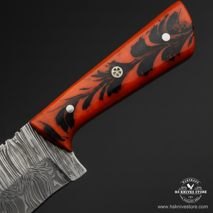 Macro view of orange resin handle with black floral leaf inlay design and silver pin on Damascus skinner knife