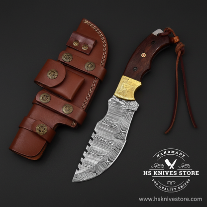 Damascus steel tracker knife with brass engraved bolster and wood handle and leather sheath on dark charcoal background studio shot