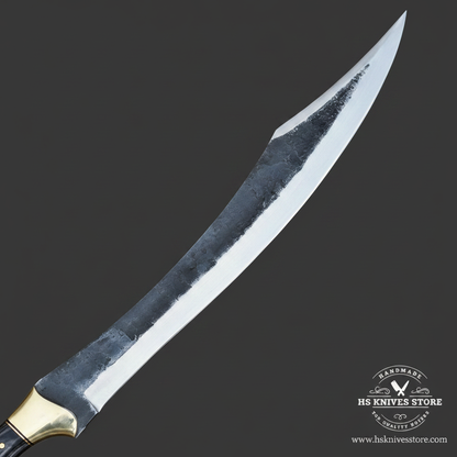 Macro view of the two-tone brute-de-forge finish and polished edge on a curved carbon steel Falcata blade