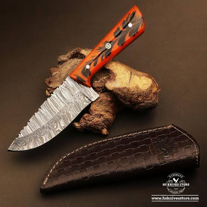 Damascus steel skinner knife with orange resin handle and crocodile leather sheath on dark charcoal background