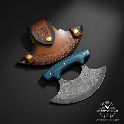 Damascus ulu knife with blue pakkawood handle and crescent leather sheath on dark charcoal studio background facing right