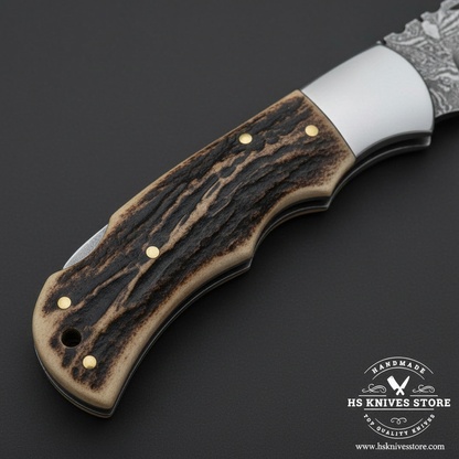Macro view of natural stag antler handle with brass pins and clean stainless steel bolster on Damascus folding knife