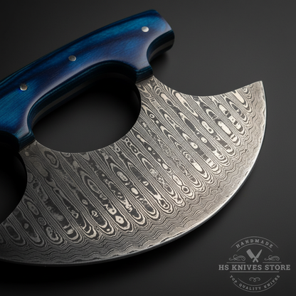 Macro close-up of Damascus steel ulu knife wide crescent blade showing bold wavy flowing pattern and open thumb hole