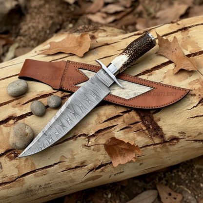 Damascus Bowie knife with stag horn handle and tan leather sheath flat lay on rustic wood log