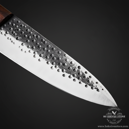 Close-up of carbon steel chef knife blade showing hand-hammered dimple honeycomb dot texture and dark hammered spine macro detail