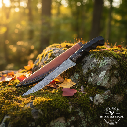Damascus steel fillet knife with ebony honeycomb handle and two-tone leather sheath on mossy rocks in forest setting