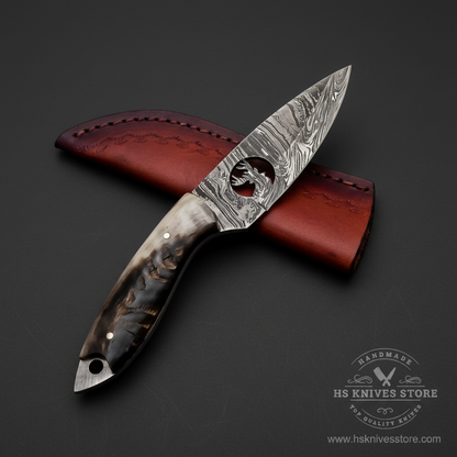 Damascus steel skinner knife ram horn handle thumb hole blade dark burgundy leather sheath dark charcoal studio mirror