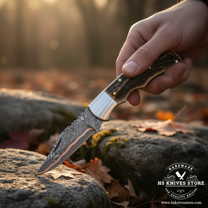 Hand holding open Damascus folding pocket knife with stag handle in outdoor action shot with golden light