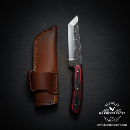 Carbon steel skinner knife with red black pakkawood handle and brown leather sheath displayed vertically on dark slate luxury studio background