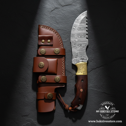 Damascus steel tracker knife displayed vertically on dark slate with brass bolster wood handle and leather sheath luxury shot