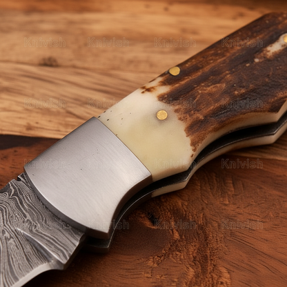 Close-up macro of stag antler handle and polished steel bolster on Damascus back lock folding knife