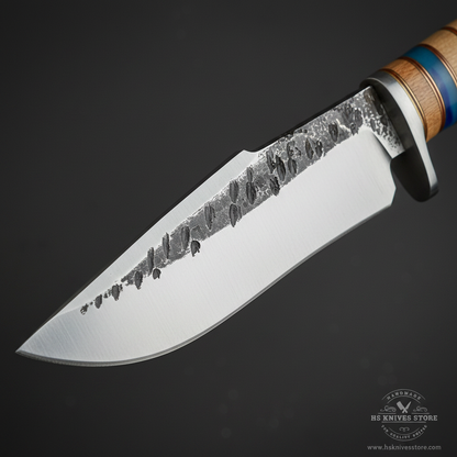 Close-up macro of hand forged stainless steel blade showing hammered textured spine and polished flat with silver bolster guard