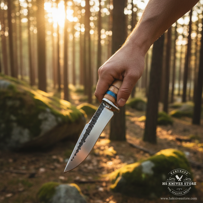 Hunter hand gripping stacked maple wood blue resin handle hand forged hunting knife in action pose outdoor forest golden sunlight