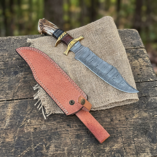 Outdoor display of Damascus Bowie and reddish-tan sheath on burlap