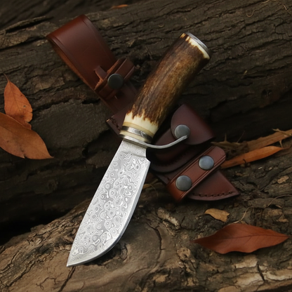 Damascus hunting knife with stag antler handle flat lay on rustic dark wood surface with brown leather sheath and dried leaves