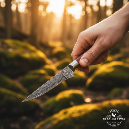 Hand gripping red hardwood handle Damascus skinning knife with brass medallion in outdoor forest action shot with golden hour light
