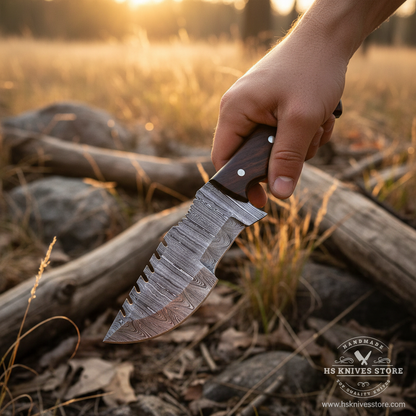 A hand holds a large fixed-blade knife outdoors in a grassy field at sunset. The knife has a patterned Damascus-style steel blade and a dark wooden handle with metal rivets.