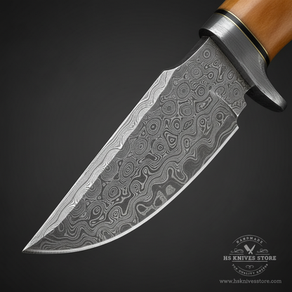 Close-up macro of Damascus steel skinner blade showing swirling layered Damascus pattern and finger choil at ricasso