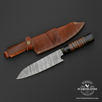 Damascus chef knife with buffalo horn wood handle and embossed leather sheath on dark charcoal background studio shot