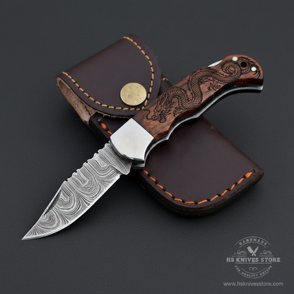 Damascus steel folding pocket knife open blade dragon engraved rosewood handle polished steel bolster dark charcoal studio background