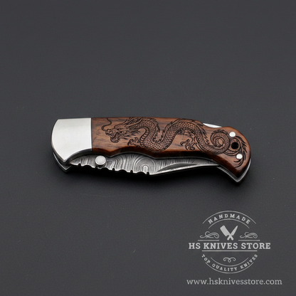 Damascus steel folding pocket knife fully closed showing dragon engraved rosewood handle and polished steel bolster back lock spine